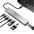 Hub USB-C argent connecté à un ordinateur portable, avec ses ports et des exemples de câbles, cartes mémoire et clé USB